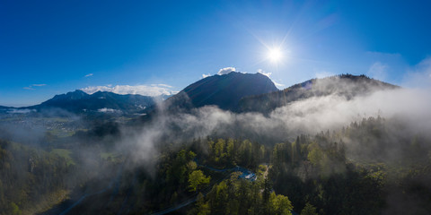 sunrise sunbeams over foggy mountains with clouds between forest trees in austria