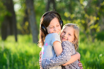 portrait of two happy adorable little girls sisters on green grass at sunny spring day. Portrait of young sisters hugging  outdoors in a park.