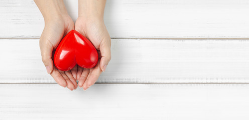 Woman Hands Hold Red Heart on white wood background. Protect Love or Health Concept with Copy Space.