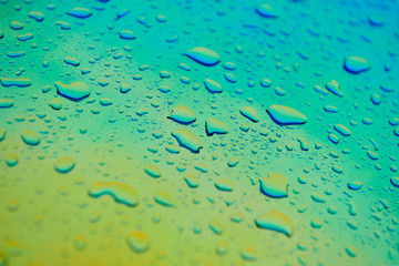 Water drops on the chameleon holographic surface. Beautiful colorful background with shallow depth of field. Blue and yellow gradient. Closeup.