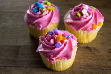 Closeup of cupcakes decorated with pink icing and sprinkles on a dark wooden background