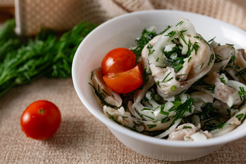 Marinated oyster mushrooms, garnished with cherry tomatoes and green dill. A dish with onions and butter in a white plate with a beige light cloth on the table