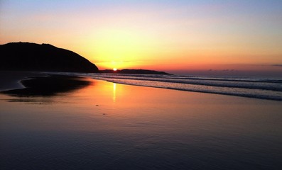 Atardecer en la playa, el sol muy anaranjado se refleja en el agua de la orilla de la playa