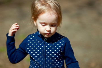 Adorable shaggy toddler girl wearing deep blue woolen jacket outdoors in a sunny spring day