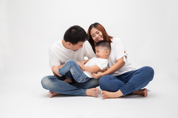 Naklejka na ściany i meble Cheerful Asian family sitting over white background have fun father tickling little son. Young couple with kids wearing white top and blue jeans. Parents enjoy free time playing concept