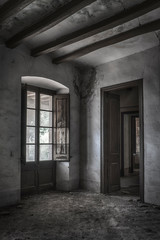 Habitación sucia con ventana y puerta en la penumbra de casa de campo abandonada en ruinas. 