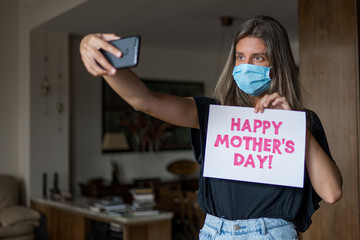 Chica rubia con mascarilla haciéndose un selfie para felicitar el día de la madre durante el confinamiento de COVID-19.