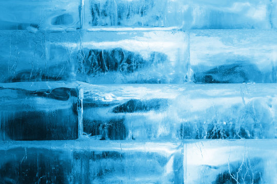Large pieces of ice made in the form of a brick wall, transparent, illuminated by blue light. Structure, texture, background.
