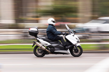 Motocicleta tipo scooter a gran velocidad por la ciudad conducida por un ejecutivo