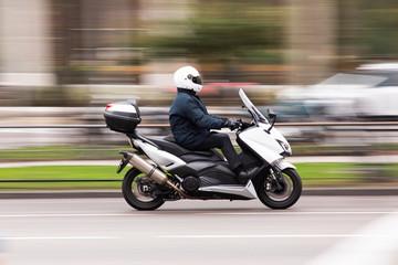 Motocicleta tipo scooter a gran velocidad por la ciudad conducida por un ejecutivo © miguel