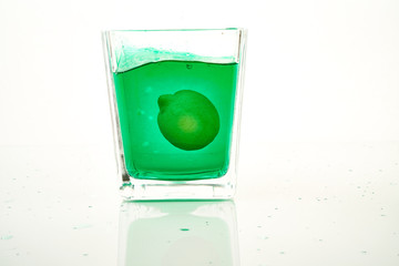 glass of green cocktail with lemons on white background