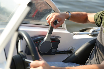 male hand is on the control lever of a white motor boat close up
