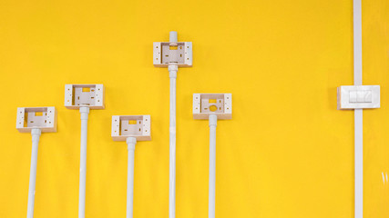 White plastic light switch box with pipe line and electric socket boxes on yellow cement wall background inside of house construction site