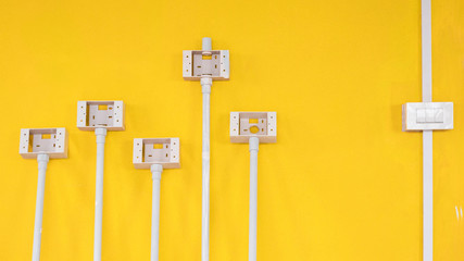 White plastic light switch box with pipe line and electric socket boxes on yellow cement wall...