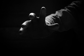 Front view of the scary hand of mysterious criminal in black glove reaching from the dark background in low key style, concept for mystery, crime,danger, threat and horror - obrazy, fototapety, plakaty