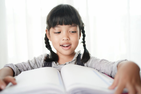 Asian little child girl reading the books to review the knowledge that teachers teach from school. School children love to read and education concept.