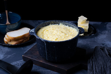 Corn porridge with milk in a black saucepan against the dark background