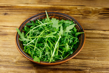 Obraz na płótnie Canvas Fresh green arugula in ceramic bowl on a wooden table. Healthy food or vegetarian concept