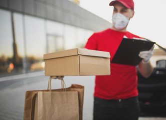 Deliveryman in red uniform with brown paper package in medical respirator in vehicle