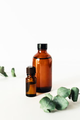 Two bottles of fragrant cosmetic or essential oil on a white background surrounded by sprigs of...