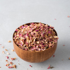 Dried tea rose petals in a wooden bowl on white background.