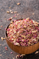 Dried tea rose petals in a wooden bowl on dark background.