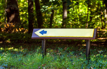 A small left arrow in a park or forest. Pointer among green plants.