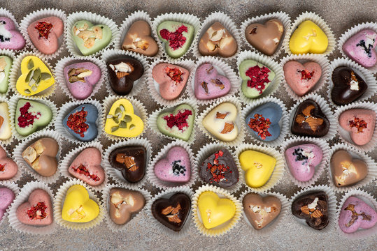 Handmade colored heart-shaped chocolates with nuts and dried fruits and berries. Candy background.
