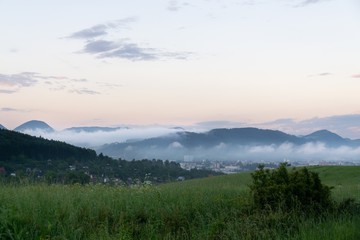 Obraz premium Sunrise and sunset, beautiful clouds over the meadow, hills and buildings in the town. Slovakia