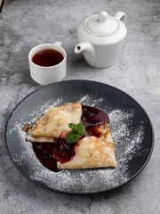 Crepes with cherry jam folded in triangles decorated with powdered sugar, on black plate, close mouthwatering shot