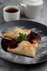 Crepes with cherry jam folded in triangles decorated with powdered sugar, on black plate, close mouthwatering shot