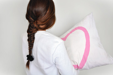 Chica de espaldas con una trenza abrazando la almohada. Fondo blanco.