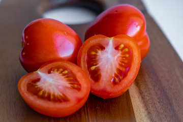 Two whole tomato and two halves of tomato isolated on a wooden cutting board on white background,...