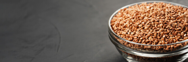 Buckwheat in a glass bowl at the edge of the frame near the copy space on a black abstract background.