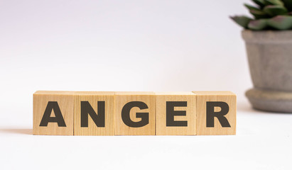 The word ANGER is made up of wooden cubes on a light background