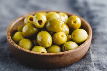 Green olives in a wooden bowl on a table, macro photography.