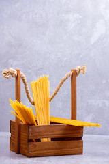 Pasta in a wooden box. Donation wooden box with raw spaghetti on a gray background. Social assistance with food. Safe food delivery. Food donation concept. Copy space