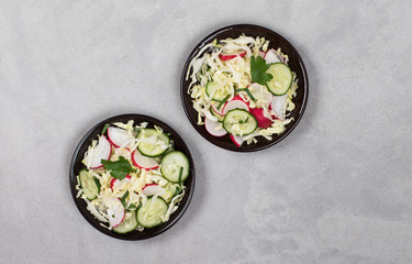Vegan salad with fresh vegetables cabbage, radishes, cucumbers and parsley on a plate on a light background top view