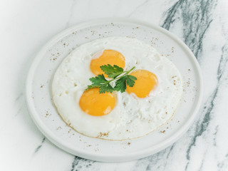 Breakfast is three eggs fried on a white plate on a white marble background. Decorated with parsley. Scrambled eggs with cheese. Photo for the menu.