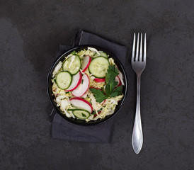 Vegan salad with fresh cabbage, radish, cucumber and parsley in a bowl on a dark gray background top view