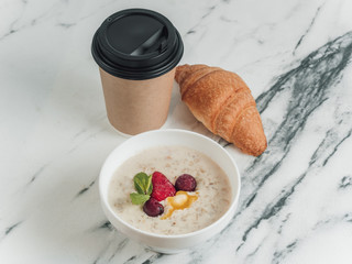 Healthy breakfast. Porridge with milk and berries. Fresh croissant. Tea or coffee in a disposable...