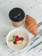 Healthy breakfast. Porridge with milk and berries. Fresh croissant. Tea or coffee in a disposable Cup. On a white marble background. The food assortment is calculated in calories. Take with you. 