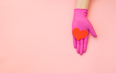 Heart symbol lies on a female hand in a medical glove on a pink background. Banner with copy space for cosmetics information, treatments and thanks.