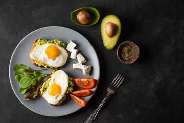 Healthy breakfast- sandwich prepared with guacamole, pepper and fried eggs with feta cheese and avocado on grey background