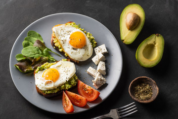 Healthy breakfast- sandwich prepared with guacamole, pepper and fried eggs with feta cheese and avocado on grey background