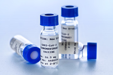 Coronavirus Covid 19 vaccine concept - small glass vials with blue caps on white table, closeup detail (own sticker design with dummy data - not real product)