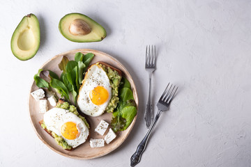 Healthy breakfast- sandwich prepared with guacamole, pepper and fried eggs with feta cheese and avocado on grey background