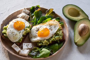 Healthy breakfast- sandwich prepared with guacamole, pepper and fried eggs with feta cheese and avocado on grey background