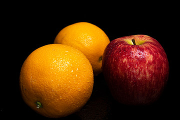 Arrangement with fruits on a shiny black surface with black background.
