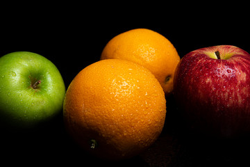 Arrangement with fruits on a shiny black surface with black background.
